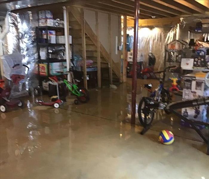 flooded unfinished basement filled with toys, and filled storage totes on shelves. 