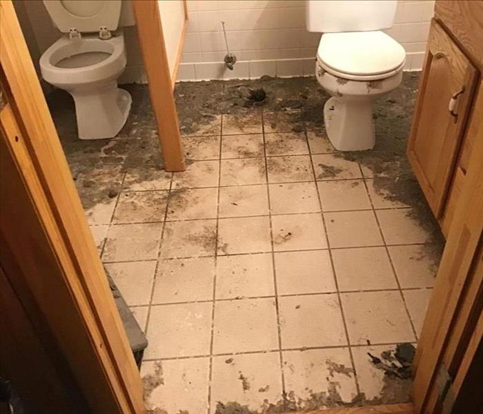 Two restroom stalls with sewage that had backed up out of the toilet bowl and into the floor.